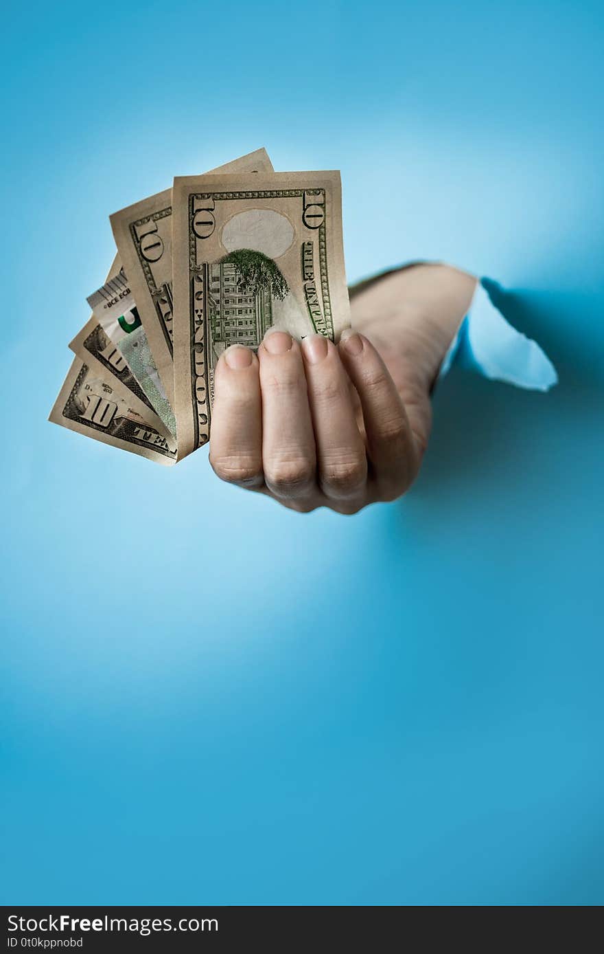 Woman hand with dollars through a hole in paper on blue background