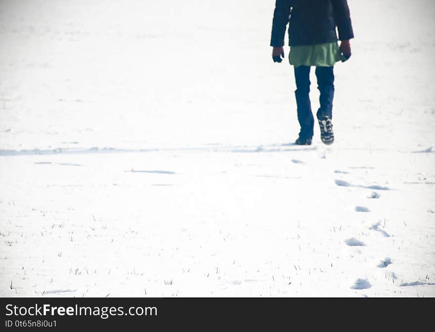 A person walking in fresh snow and making his foot marks in the snow. It is a boy in blue jeans and shoes.