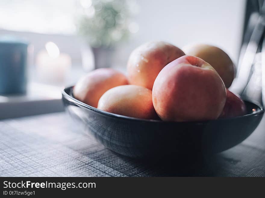 A plate of peaches on the table in front of the white windowsill.