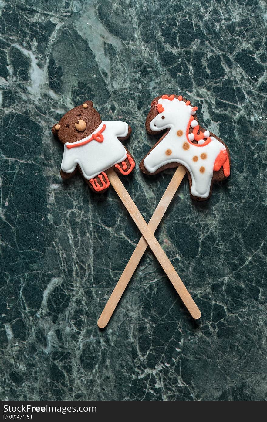 Cookies bear and horse on the stick on green marble background view from above