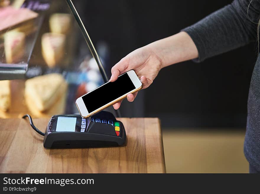 Contactless payment method. The girl applies the phone to the banking terminal. Female customers using the cell phone to pay for goods. Contactless payment method. The girl applies the phone to the banking terminal. Female customers using the cell phone to pay for goods.