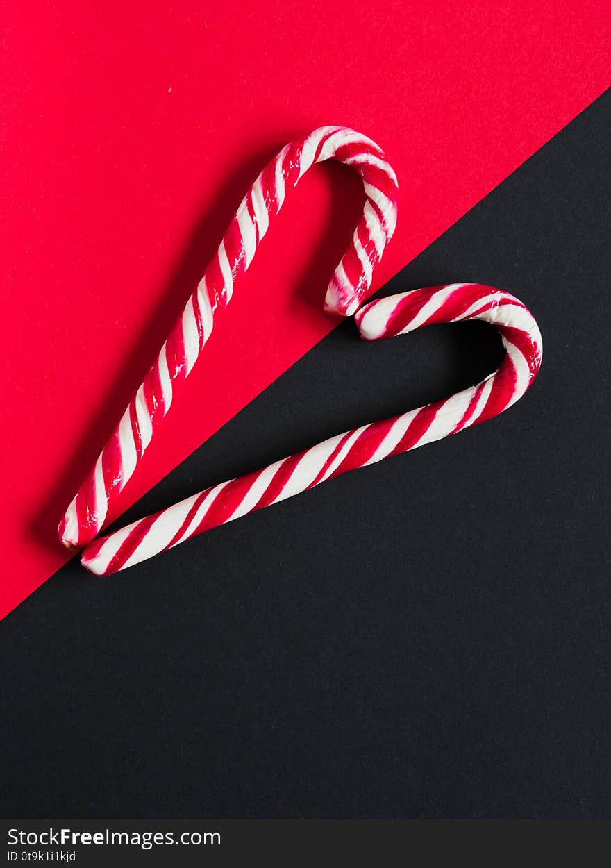 Red candy canes folded in the form of a heart on a contrasting red and black background. Top View. Photo for your postcard. Festive concept for New Year and Christmas. Red candy canes folded in the form of a heart on a contrasting red and black background. Top View. Photo for your postcard. Festive concept for New Year and Christmas