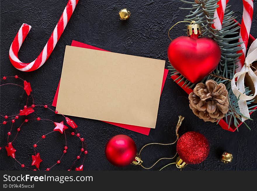 Red gift box with a Christmas toy in the shape of a heart, fir branches, christmas candy, garland , card for congratulatory text  on the black background. Top view. Flat lay. Red gift box with a Christmas toy in the shape of a heart, fir branches, christmas candy, garland , card for congratulatory text  on the black background. Top view. Flat lay