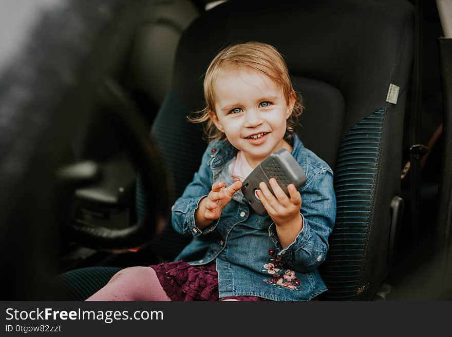 Little girl in a car seat. Holding phone in her hand. Taking driver seat. Car damage. Authentic image, child, safety, person, protection, transportation, belt, travel, childhood, security, vehicle, baby, toddler, happy, sitting, automobile, ride, buckle, care, inside, secure, young, kid, cute, caucasian, people, summer, buckled, female, interior, passenger, smiling, family, infant, booster, carseat, 4, springtime, 3, blond, blue, car-seat