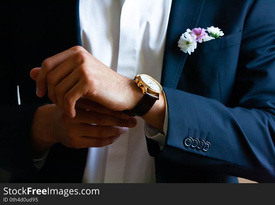 Closeup on the hands of the groom or groomsman putting on or adjusting a watch on the day of the wedding celebration, with a navy blue blazer and crisp white shirt, checking the time, getting ready, dressing up. Closeup on the hands of the groom or groomsman putting on or adjusting a watch on the day of the wedding celebration, with a navy blue blazer and crisp white shirt, checking the time, getting ready, dressing up