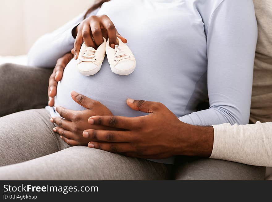 Close up of pregnant black woman belly with baby shoes on it, husband hugging his wife, new family concept. Close up of pregnant black woman belly with baby shoes on it, husband hugging his wife, new family concept