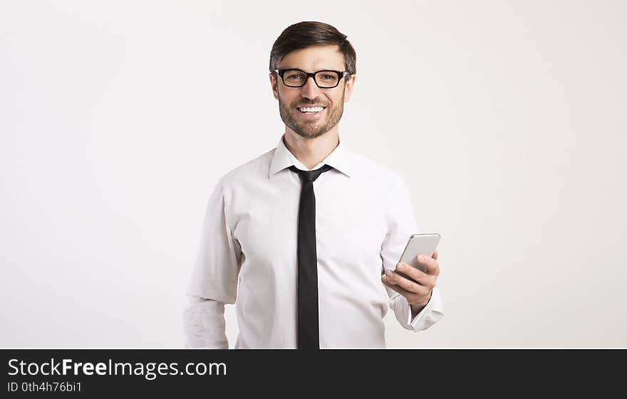 Business App. Smiling Man Using Mobile Phone Looking At Camera Standing Over White Studio Background. Panorama, Empty Space. Business App. Smiling Man Using Mobile Phone Looking At Camera Standing Over White Studio Background. Panorama, Empty Space