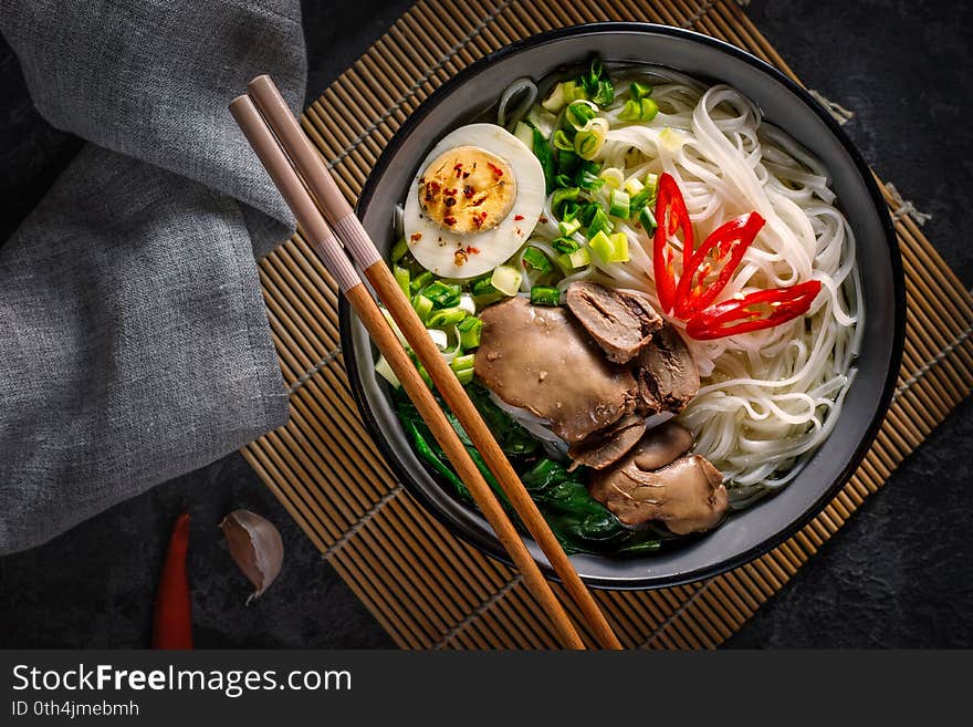 Chinese noodles with chicken giblets with an egg, green onions with lying chopsticks in a bowl