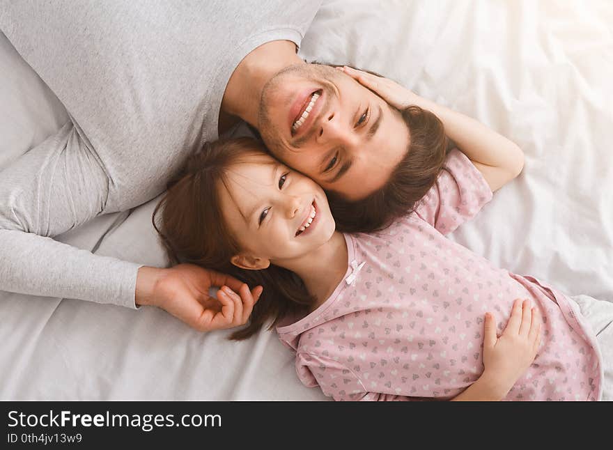 Top view of handsome young father and his cute little daughter looking at camera and smiling, lying on bed at home, just woke up, affectionate concept. Top view of handsome young father and his cute little daughter looking at camera and smiling, lying on bed at home, just woke up, affectionate concept