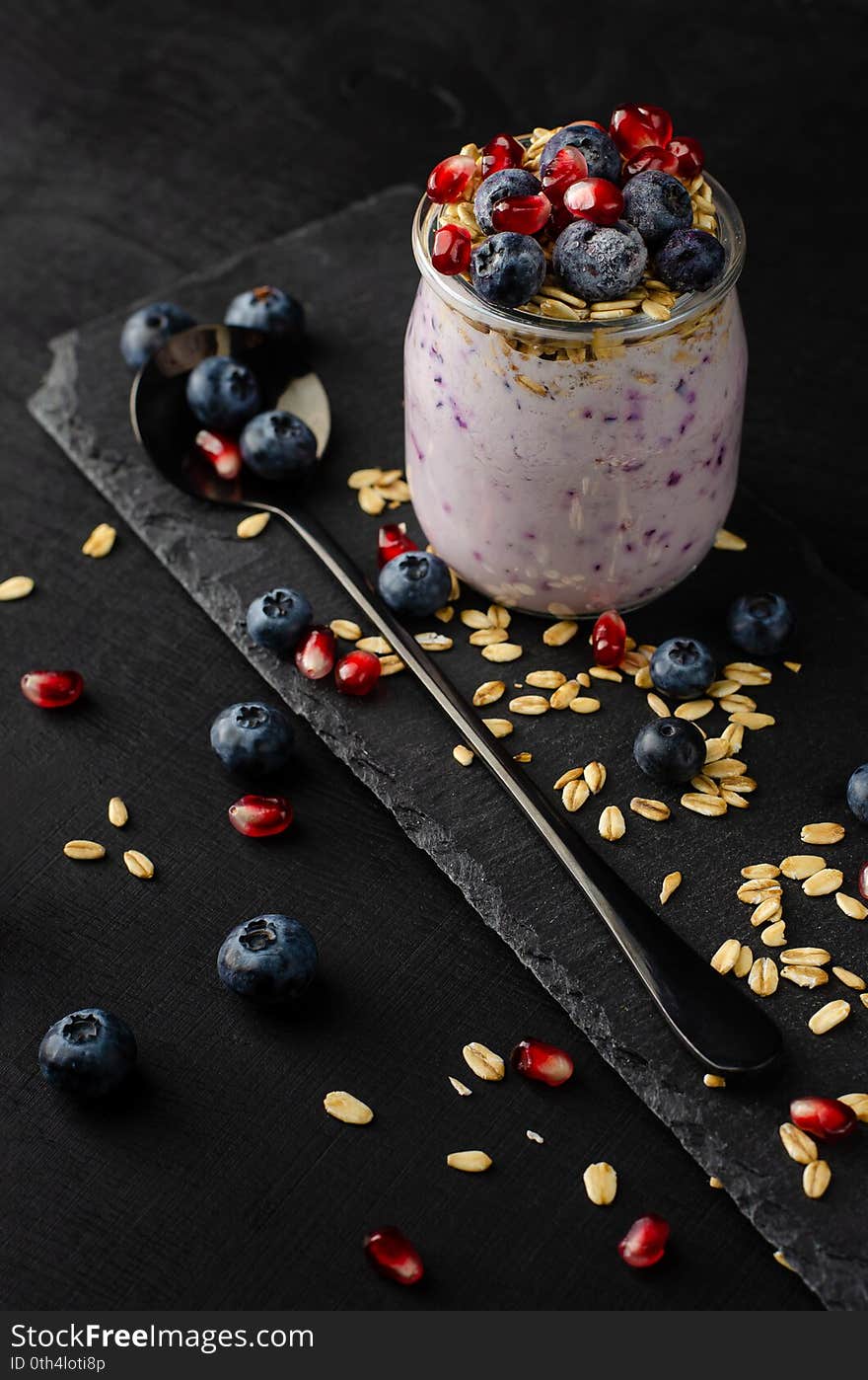 Healthy breakfast concept. Jars of homemade yogurt with blueberries, pomegranate seeds and oats on black background.