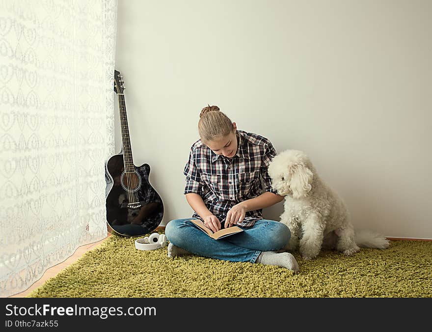 Teenager on the carpet by the window reading a book in the company of the dog. Teenager on the carpet by the window reading a book in the company of the dog