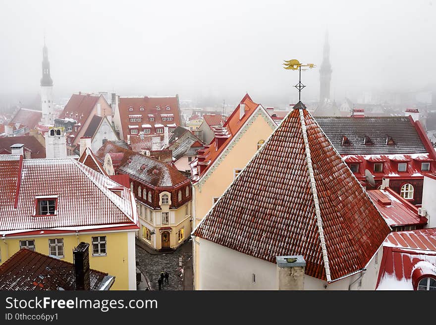 Aerial cityscape view of Tallinn Old Town on winter day. Snow covered red rooftops from tiles, Golden Cockerel weathervane, Town Hall spire, modern office buildings skyscrapers far away. Aerial cityscape view of Tallinn Old Town on winter day. Snow covered red rooftops from tiles, Golden Cockerel weathervane, Town Hall spire, modern office buildings skyscrapers far away