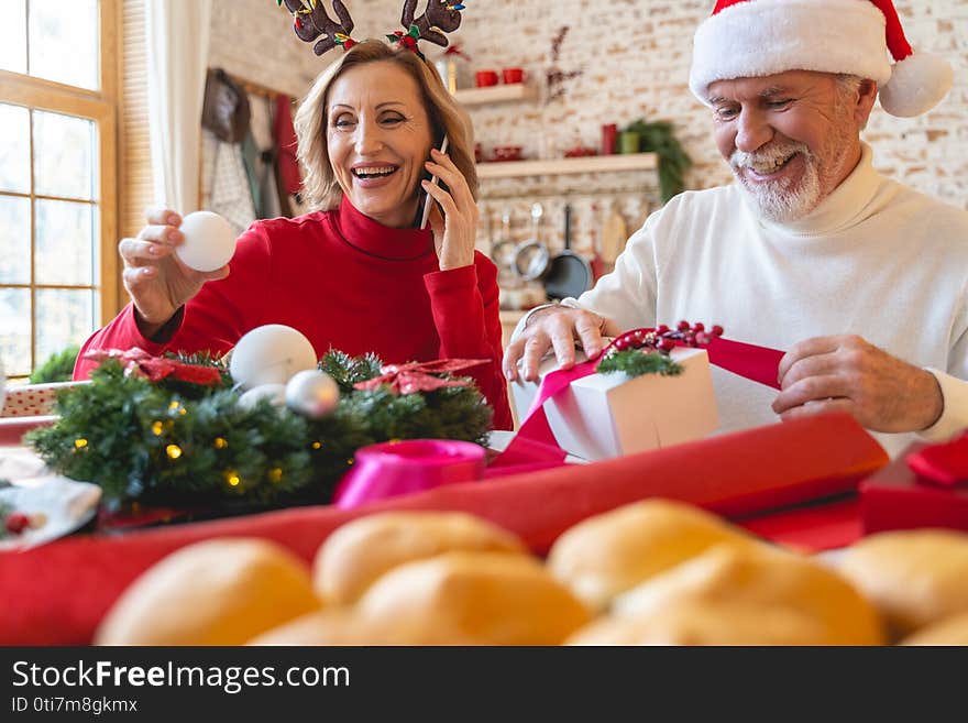 Handsome mature men sitting near his wife and wrapping presents for grandchildren. Handsome mature men sitting near his wife and wrapping presents for grandchildren