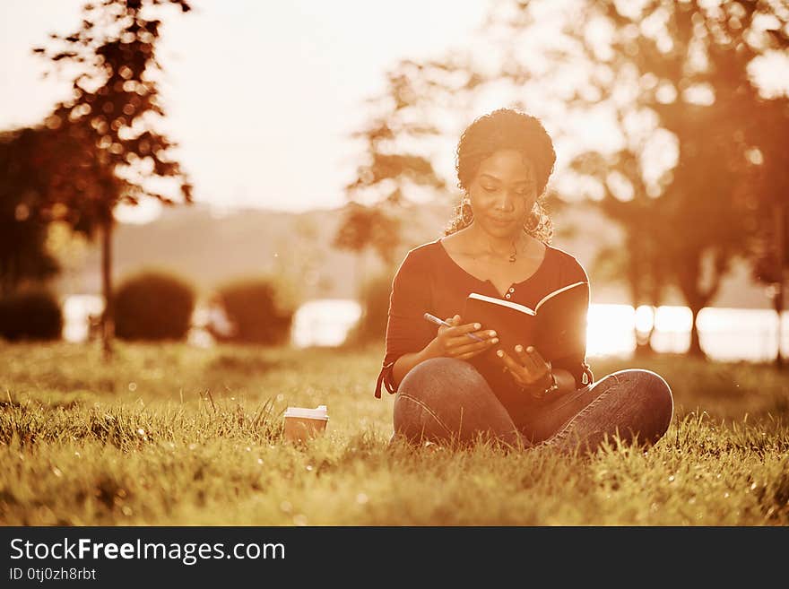 Education process. Cheerful african american woman in the park at summertime