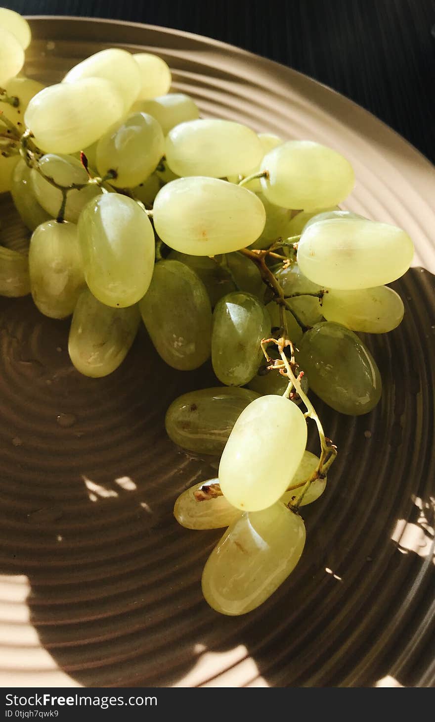 Bunch of white grapes on a plate lit by the sun. Bunch of white grapes on a plate lit by the sun.