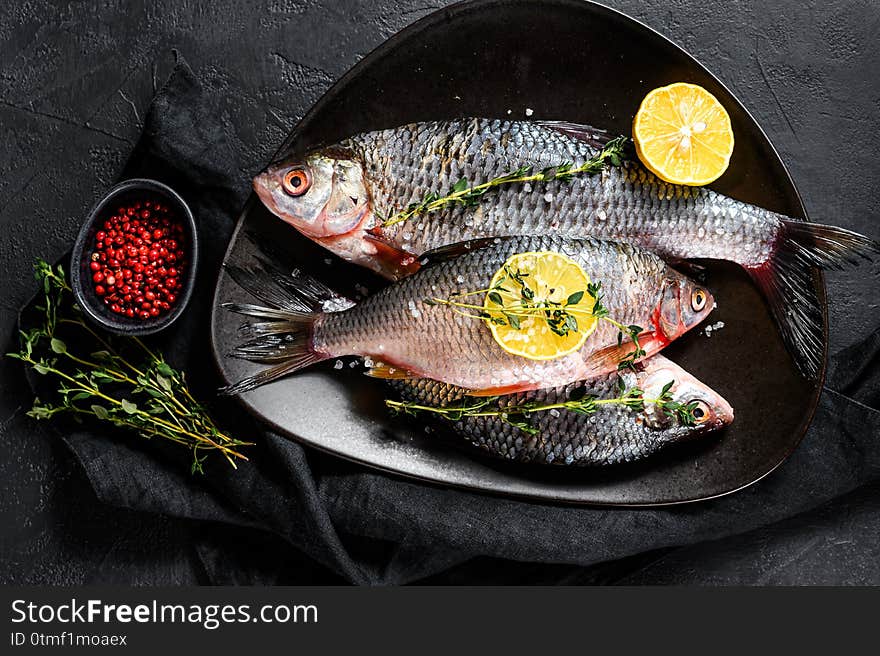 Crucian carp with lemon and thyme on a black plate. River organic fish. Black background. Top view