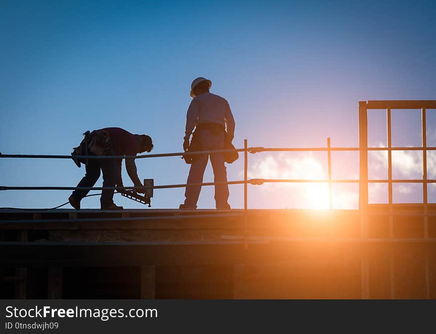 Construction Workers Silhouette on Roof of Building