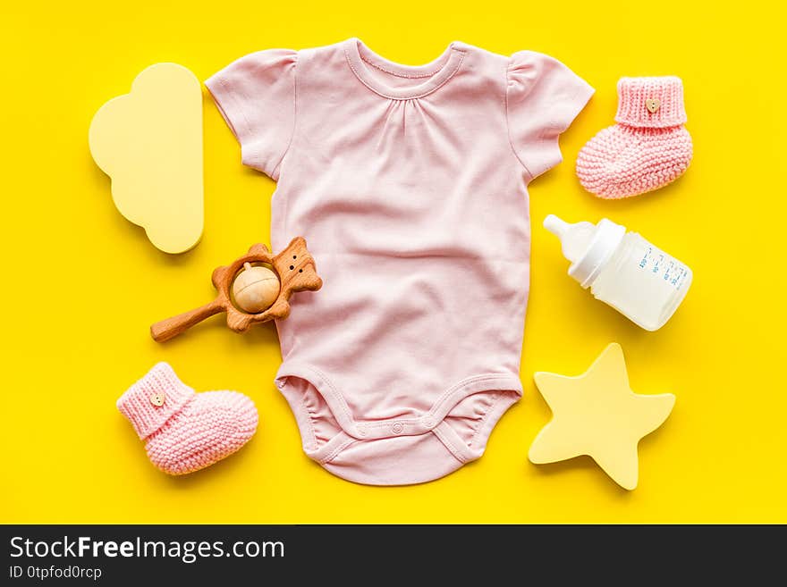 Pink bodysuit for baby girl near children`s things on yellow background top-down