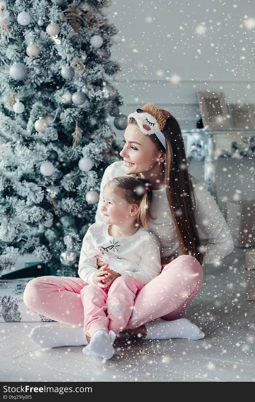 Happy festive mother and daughter hugging sitting together at decorating beautiful Christmas tree background. Smiling family posing having Xmas positive emotion at cozy home interior