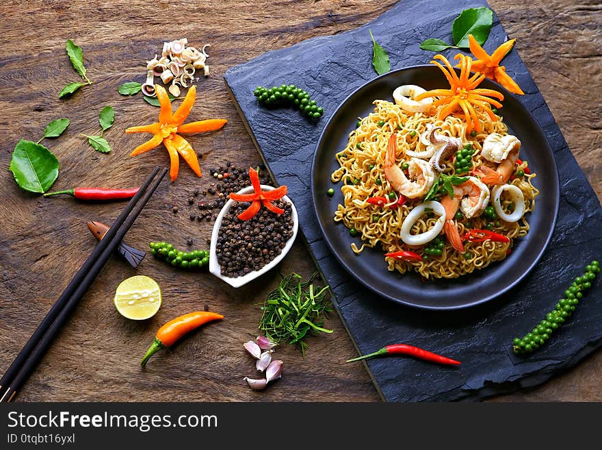 instant noodles with stir fried spicy seafood and various herbs on black stone plate