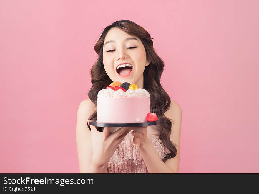 Joyful woman with cake front pink background