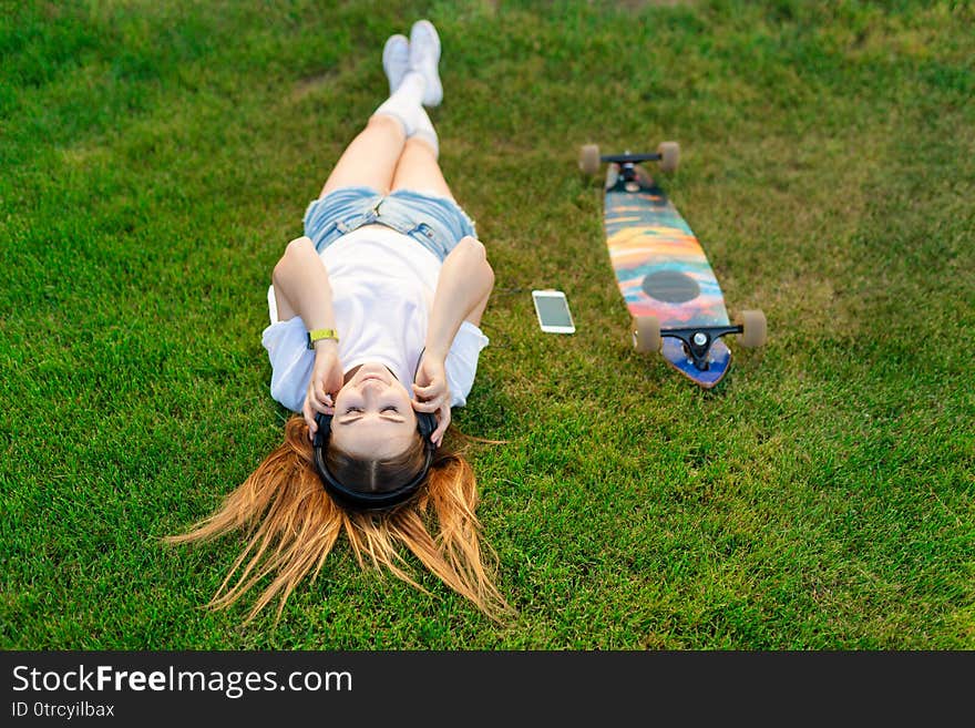 Young girl enjoy lay in green lawn and listening music after riding on her logboard.