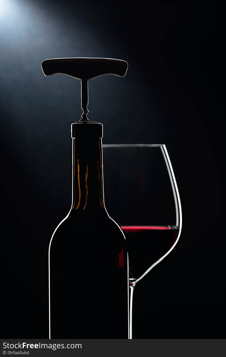 Bottle with corkscrew and glass of red wine on a dark background