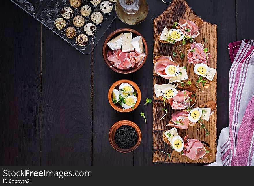 Bruschetta with prosciutto/jamon traditional Italian antipasto. Delicious snack with bread, brie cheese and quails eggs. Health food, tapas. Top view, copy space