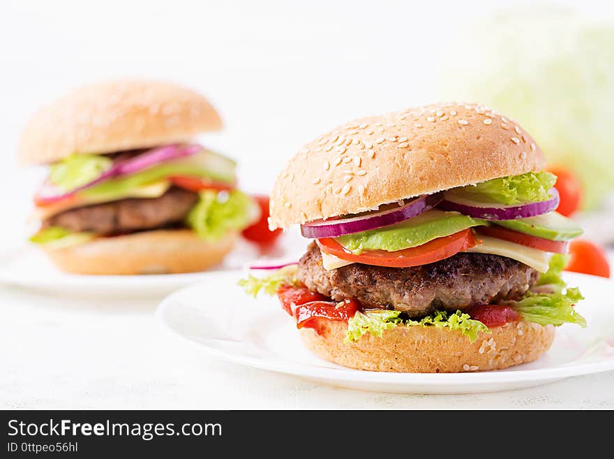 Big sandwich - hamburger burger with beef, avocado, tomato and red onions on light background. American cuisine. Fast Food