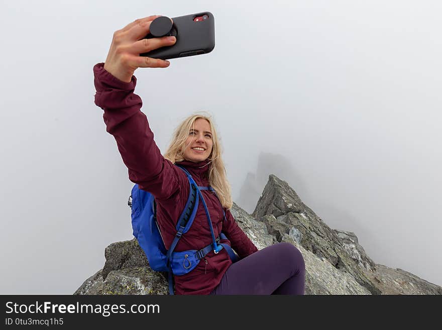 Young Adventurous Girl on top of a rugged rocky mountain taking a selfie during a cloudy summer morning. Taken on Crown Mountain, North Vancouver, BC, Canada. Young Adventurous Girl on top of a rugged rocky mountain taking a selfie during a cloudy summer morning. Taken on Crown Mountain, North Vancouver, BC, Canada
