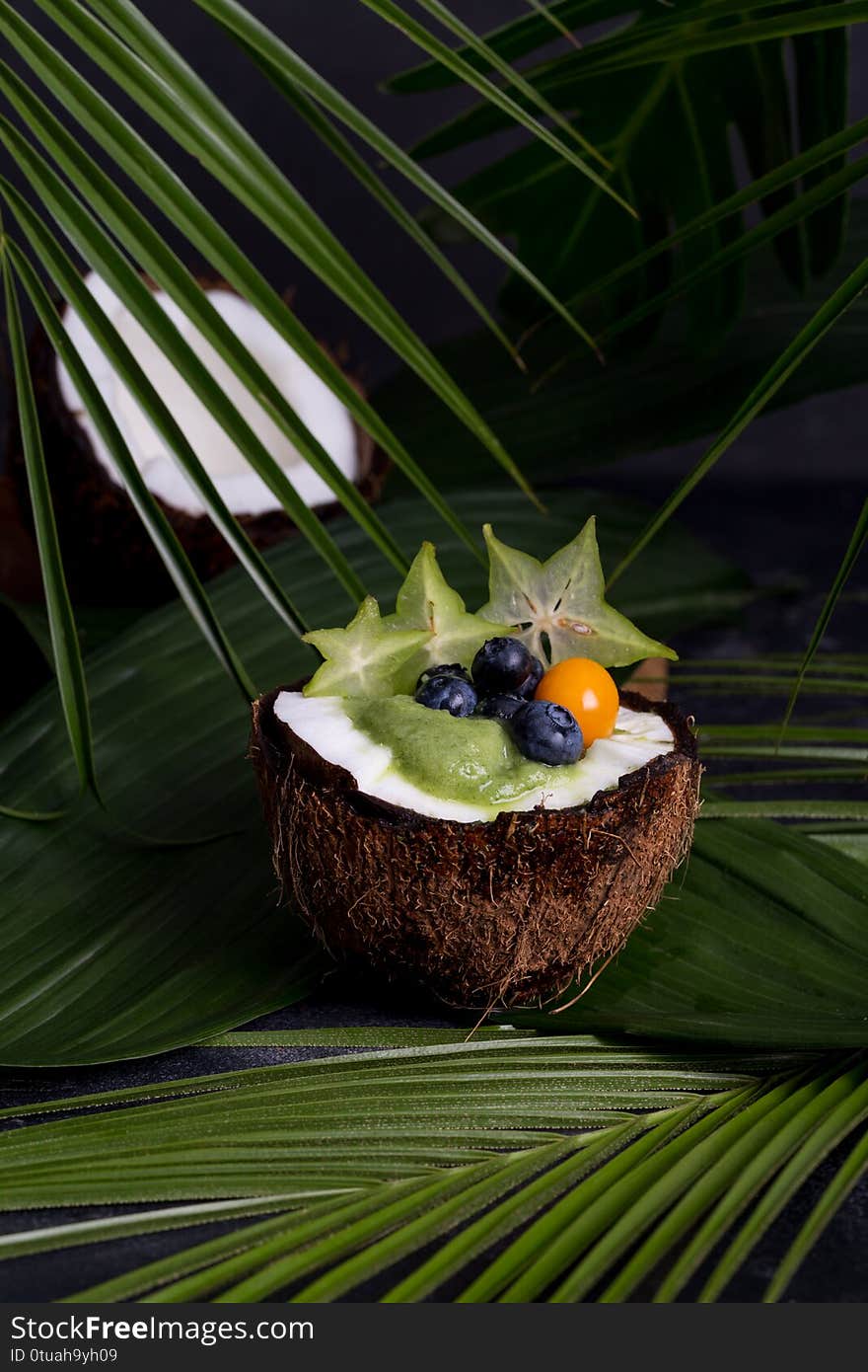 Smoothie in coconut with berries and leaves on background. Concept of tasty tropical food. Copy space for text, banner and blank