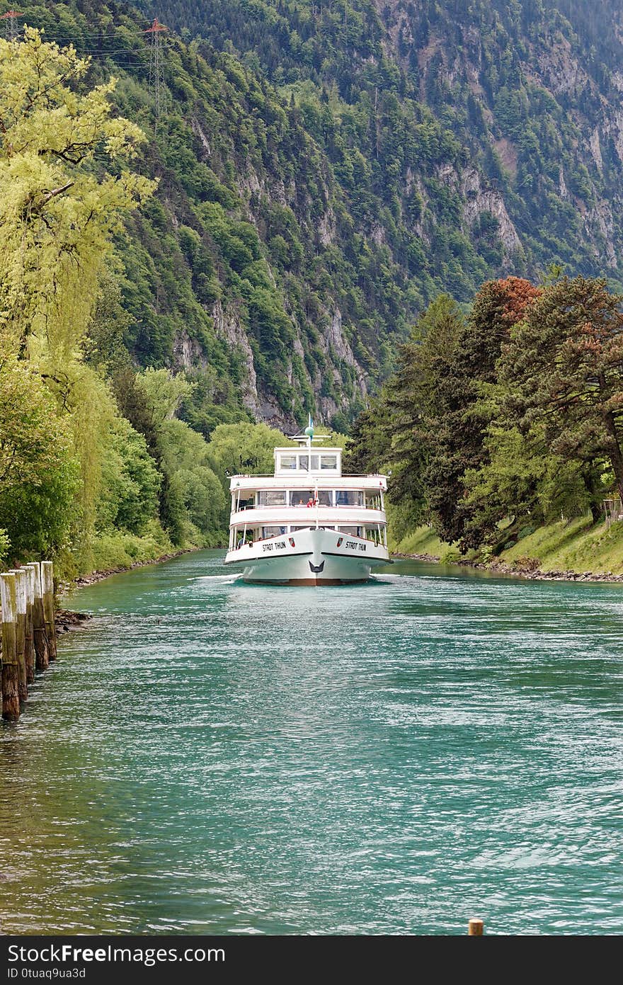 Passenger Vessel traversing the river from the Thun lake between steep verdant cliffs. Approaching its berth. Vessel takes visitors around the lake. Passenger Vessel traversing the river from the Thun lake between steep verdant cliffs. Approaching its berth. Vessel takes visitors around the lake.