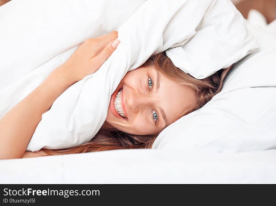 Young woman lying on bed morning at home under blanket looking camera laughing cheerful close-up. Young woman lying on bed morning at home under blanket looking camera laughing cheerful close-up