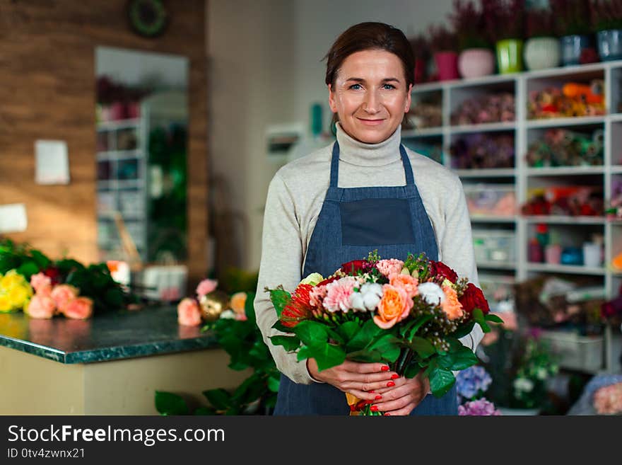 A cute flower girl in a blue apron holds a beautiful composition of flowers.