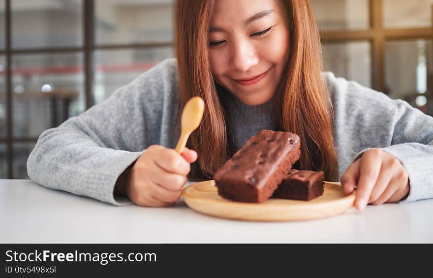 A beautiful asian woman looking and eating delicious brownie cake in wooden plate