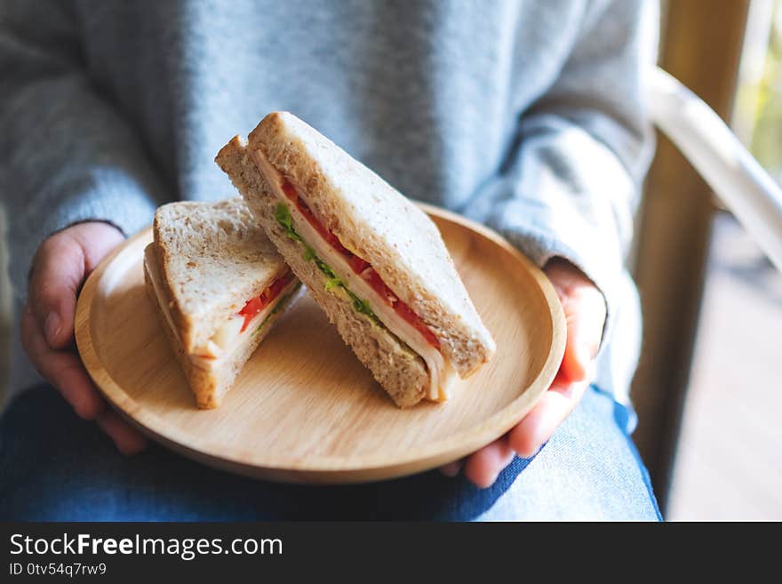 A woman holding and serving two pieces of whole wheat sandwich in wooden plate