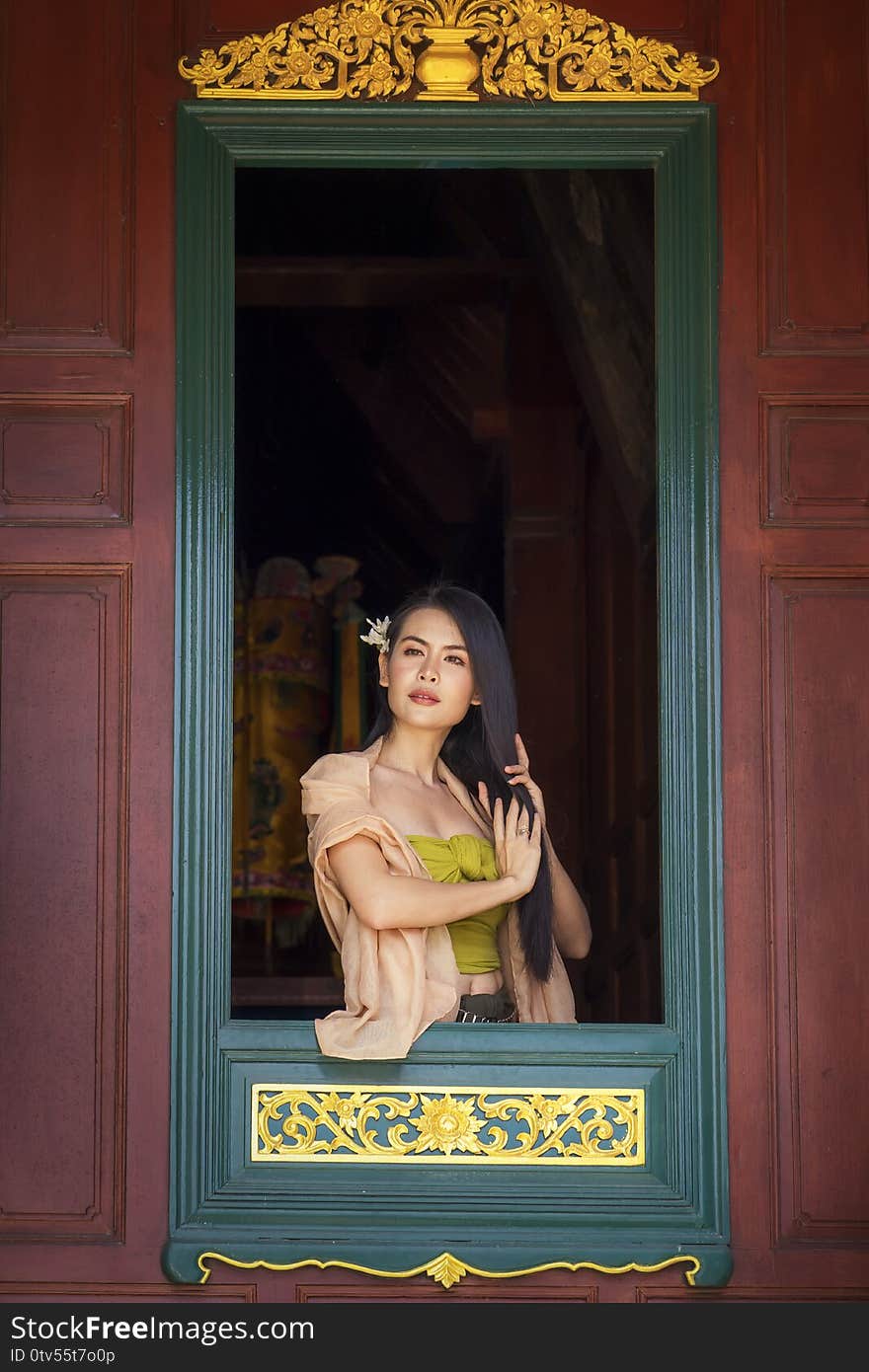 Woman wearing Thai costume combing hair in window. Asian girl wearing Thai traditional dress hand holding hair on window. looking