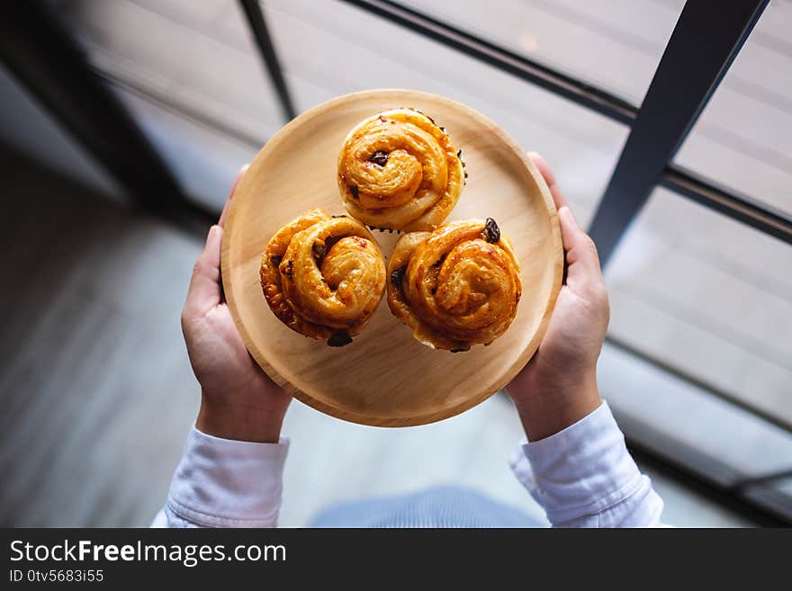 A Waitress Holding A Wooden Plate Of Raisin Danish