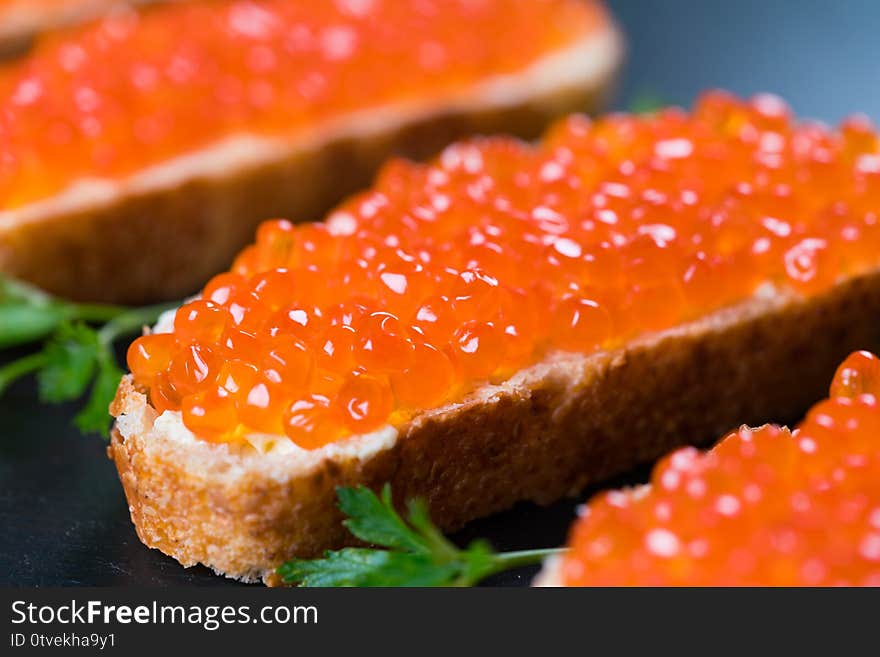 Sandwiches with red caviar on dark stone background