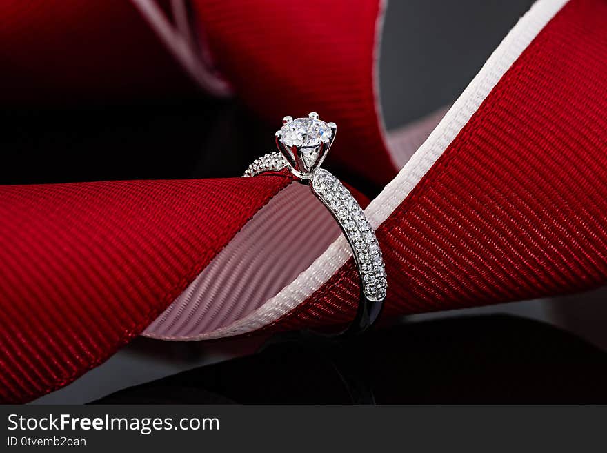 Wedding diamonds ring on black background with red ribbon. Silver engagement ring with gemstone. Advertising still life