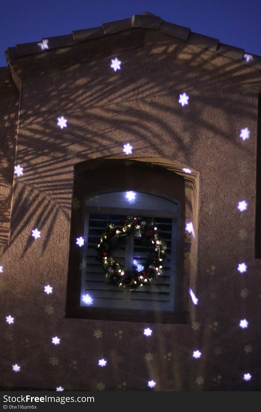 A house decorated for the holidays with a wreath and a radial snowflake pattern projection. A house decorated for the holidays with a wreath and a radial snowflake pattern projection