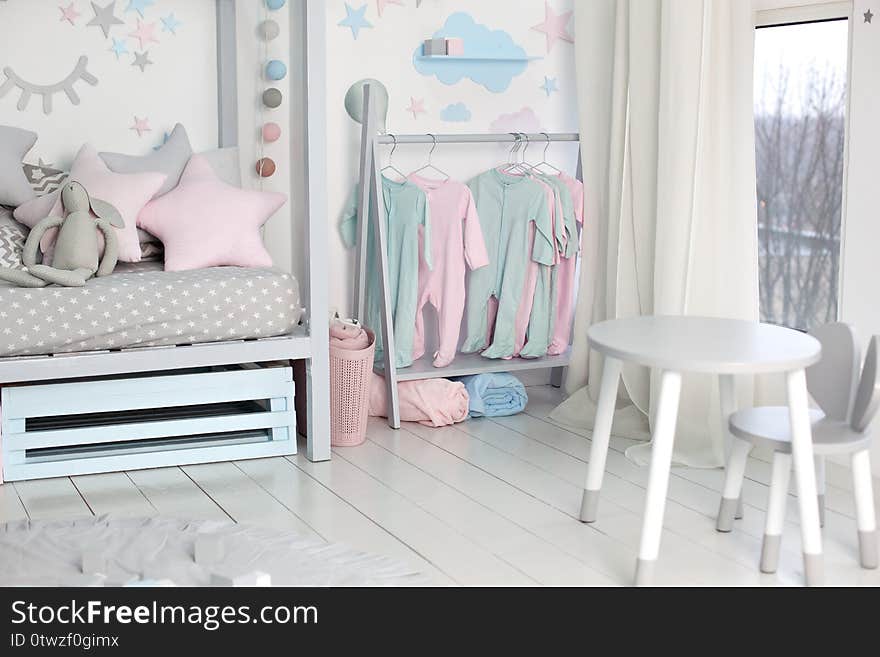 Clothes for little child hung in children room. Rack with hangers with baby clothes. Children cloth rack. Pastel color children clothes in a Row on Open Hanger indoors. Children`s bedroom.  home decor