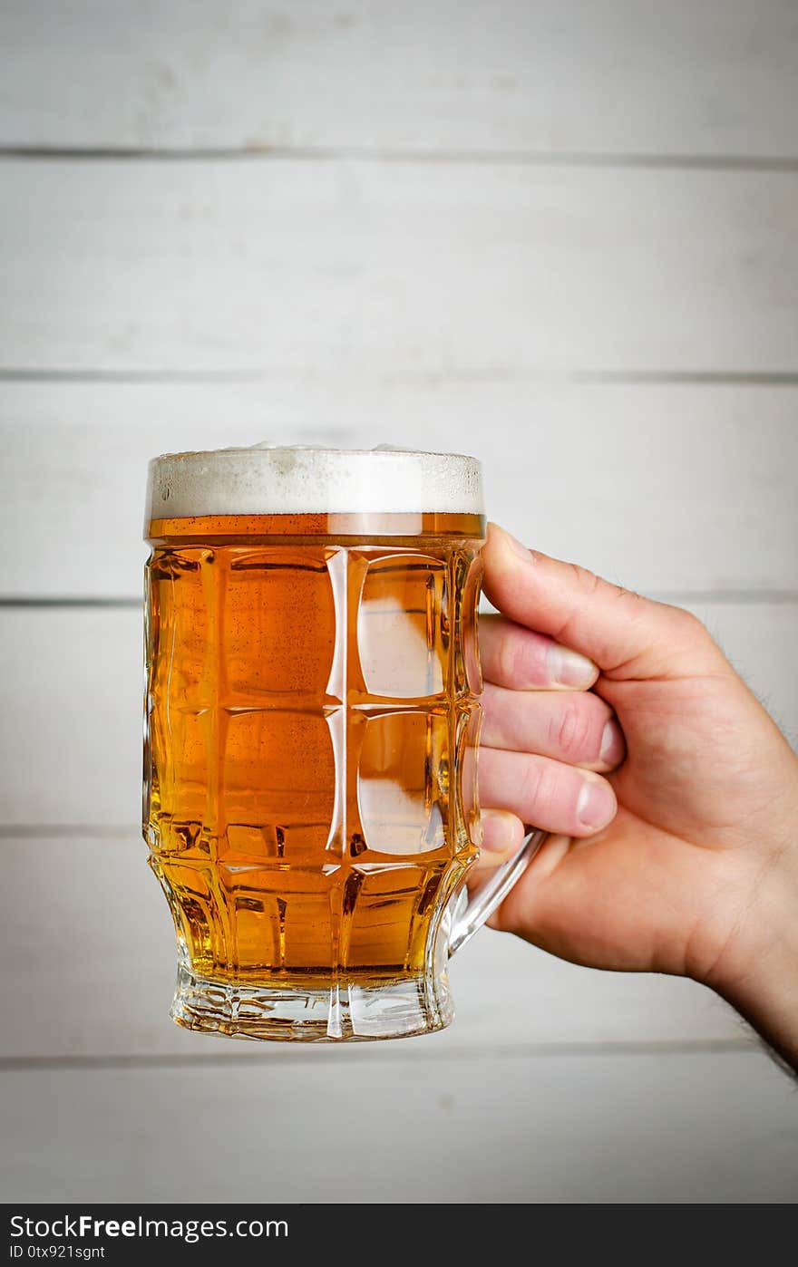 Male Hand Holding A Full Beer Mug On White Wooden Background. Toned Ima