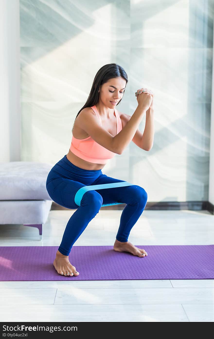 Young beautiful brunette sporty athletic woman make exercises squats with fitness elves in the loft gym