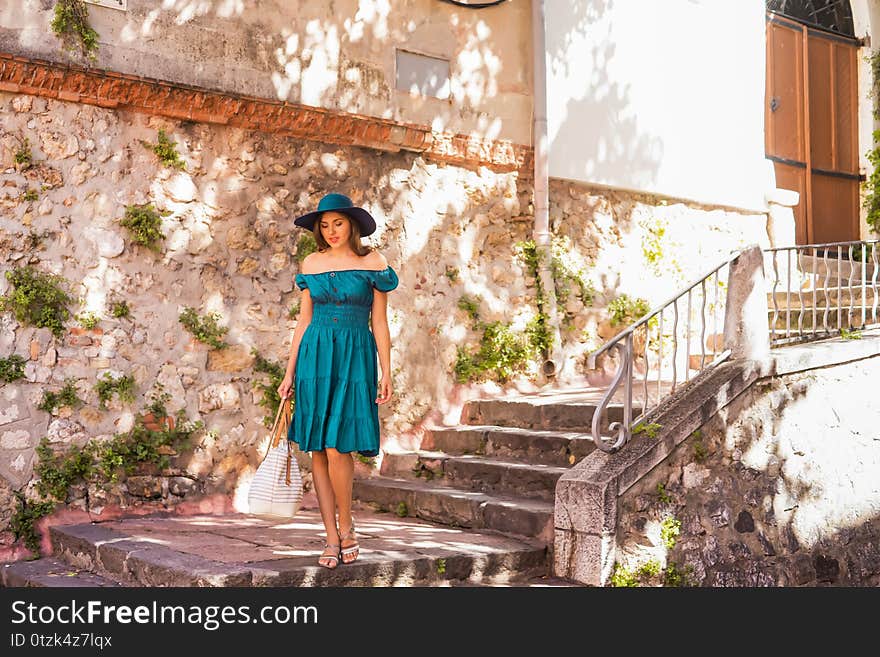 Young and beautiful brunette girl in dress and hat walking outdoor in the street. Nice, France. Summer vacation, traveling and tourism concept.