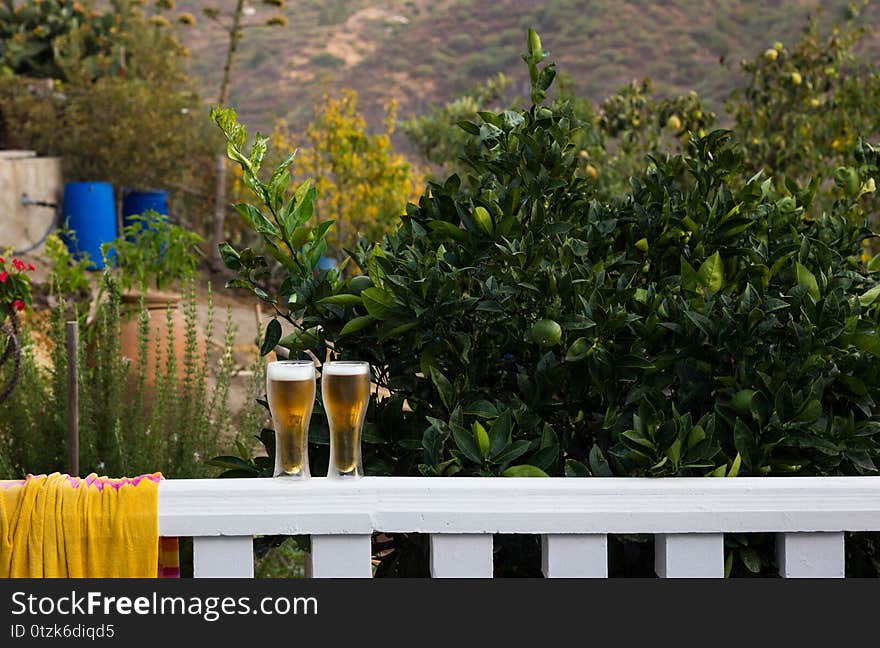 Two pints of beer on terrace white railing. Alcoholic drinks on nature outdoors. Party, celebration concepts