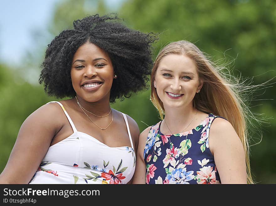 Two beautiful female friends pose for photo in park on summer day. Two beautiful female friends pose for photo in park on summer day