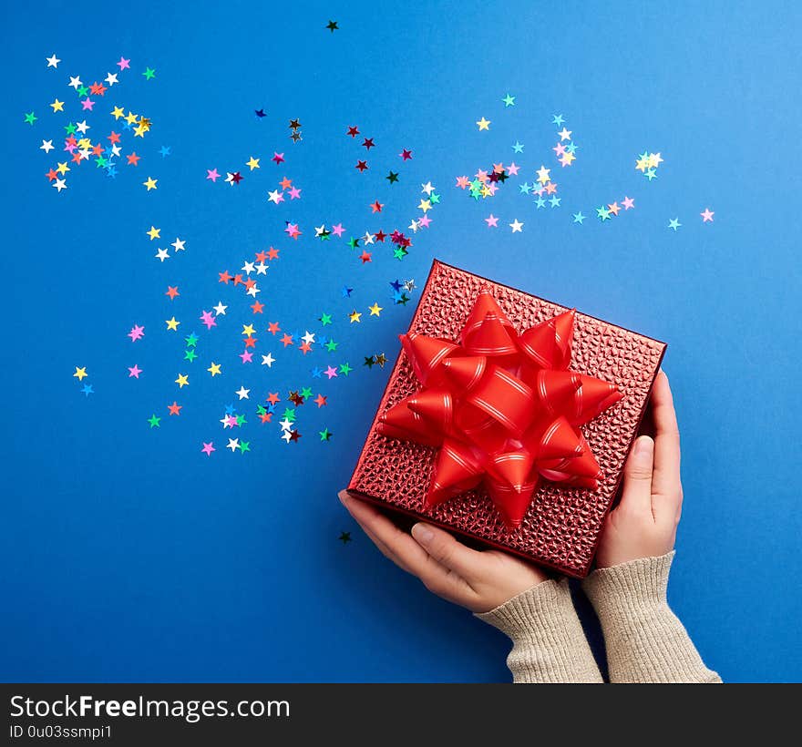 Female hands holds a beautiful shiny red box with a big red bow