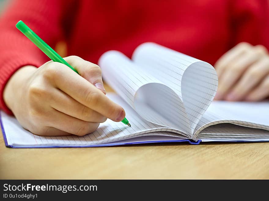 Female hand writing on a blank piece heart-shaped Notepad with pen. Female hand writing on a blank piece heart-shaped Notepad with pen