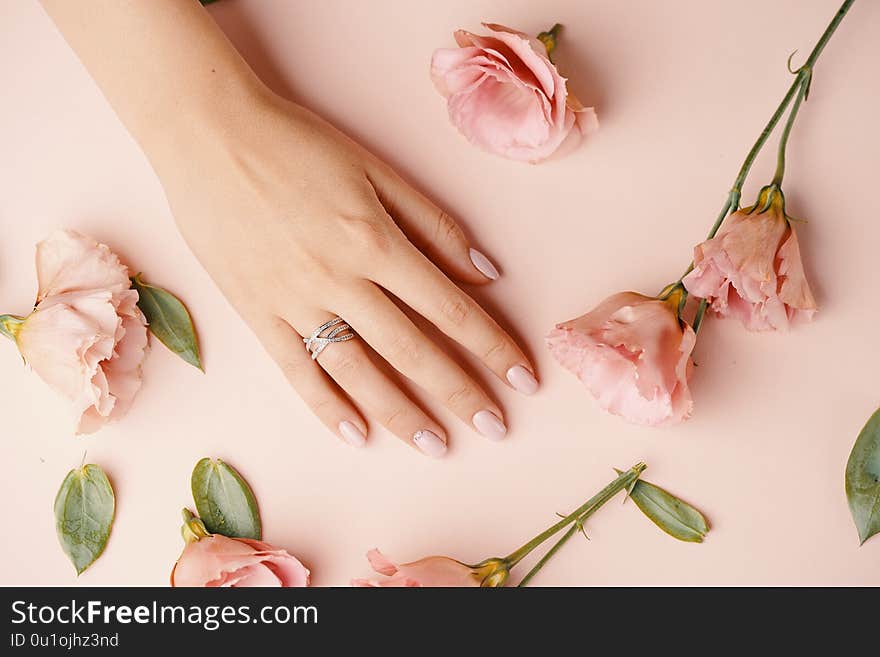 Close up of an elegant diamond ring on young woman finger. Woman hands with manicure and jewelry ring on pink background with flowers, beauty style concept. Close up of an elegant diamond ring on young woman finger. Woman hands with manicure and jewelry ring on pink background with flowers, beauty style concept.